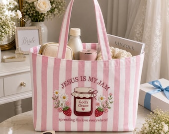 May include: A pink and white striped tote bag featuring an embroidered design of a strawberry jam jar with the text "Jesus is my jam" and "spreading His love everywhere!" surrounded by floral accents and strawberries on the front panel.
