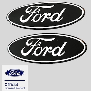 Könnte beinhalten: Zwei ovale schwarze Embleme mit dem weißen Ford-Schriftzug und einem weißen Rand. Unter den Emblemen befindet sich ein quadratisches weißes Etikett mit dem blauen Ford-Logo und dem Text Official Licensed Product in blauer und schwarzer Schrift.