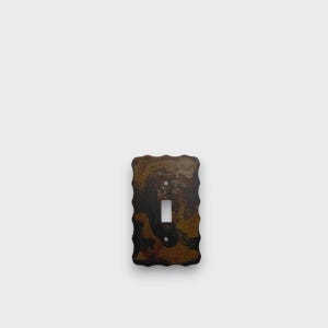 May include: A rectangular light switch cover plate with a scalloped edge and a mottled, multi-toned brown and black finish. The plate features a central vertical rectangular cutout for a toggle switch and two small circular screw holes.