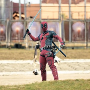 Può includere: Un costume integrale di Deadpool composto da una tuta testurizzata rossa e nera con maschera abbinata. L'abbigliamento include una cintura multiuso con tasche, ginocchiere nere e due spade color argento tenute nelle mani, una sollevata in alto.