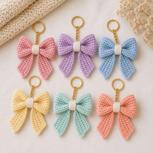 May include: Six crochet bow keychains arranged in two rows. Each bow features a textured stitch pattern in pastel colors including pink, purple, blue, yellow, mint green, and peach, with a white center knot and a gold metal keyring attached.