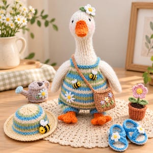 May include: A hand-knitted white goose doll wearing a blue, green, and beige striped romper with bee and daisy appliques. The goose has an orange beak and feet, a small daisy on its head, and a brown cross-body bag. Accessories include a matching striped hat, a small purple watering can, a potted flower, and blue sandals.