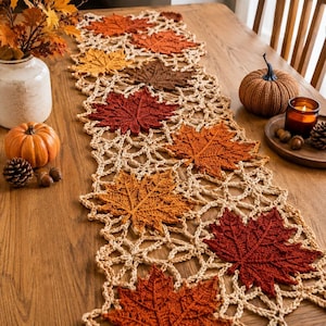 Pode incluir: Um caminho de mesa de crochê longo e retangular com um intrincado padrão de treliça vazada, intercalado com vários motivos de folhas de bordo em tons de vermelho profundo, laranja queimado, amarelo dourado e marrom, criando um design outonal.