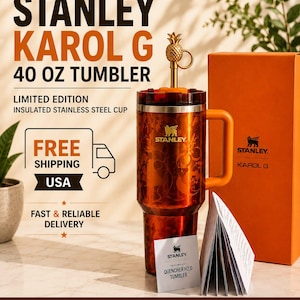 May include: A 40 oz Stanley Karol G limited edition insulated stainless steel tumbler in a metallic orange finish with a matching handle and a gold-toned pineapple-shaped straw topper. The set includes a matching orange box and a product manual.