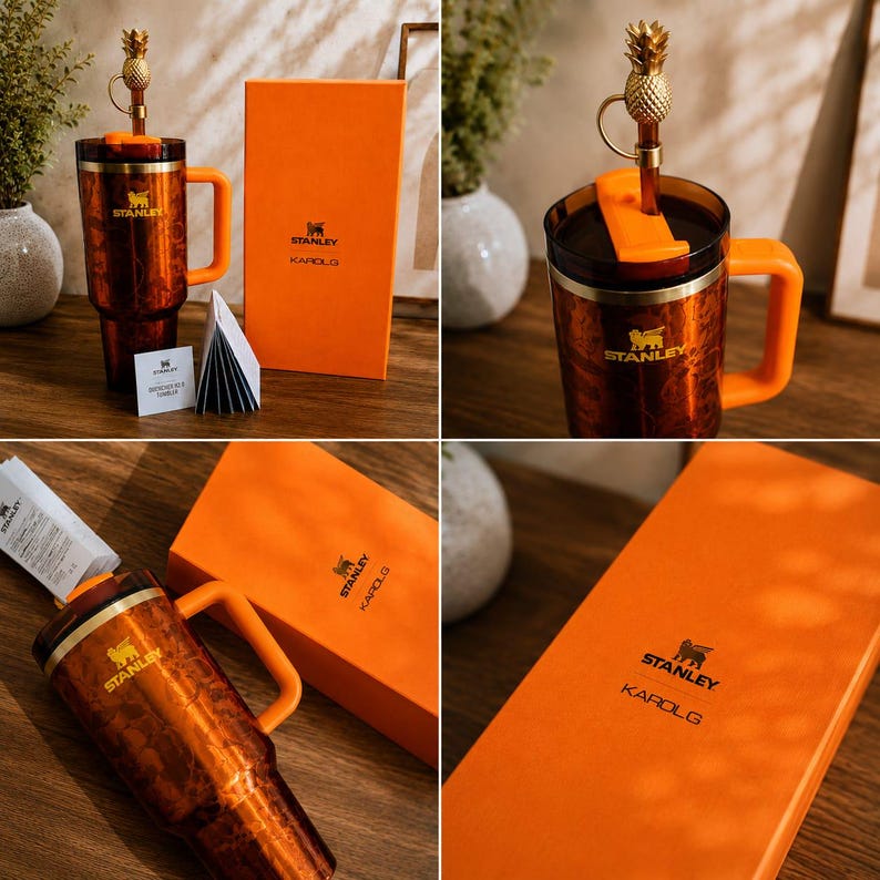 May include: A copper-colored Stanley tumbler with a handle, an orange lid, and a gold pineapple-shaped straw topper. The tumbler features the Stanley logo and is accompanied by an orange box labeled Stanley Karol G and a small informational card.