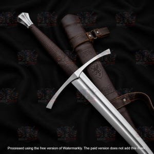 Puede incluir: Una espada larga de acero con pomo plateado, empuñadura forrada en cuero marrón y una guarda con gavilanes curvos. La espada se acompaña de una vaina de cuero marrón grabada con un emblema de grifo y herrajes metálicos.