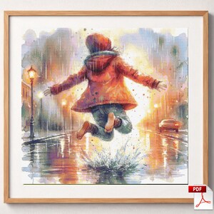 Op de afbeelding: Een ingelijst kruissteekpatroon met een aquarelillustratie van een persoon in een rode jas met capuchon die in een regenplas springt. De scène bevat een lantaarnpaal, een auto en vallende regen, uitgevoerd in levendige, zachte kleuren.