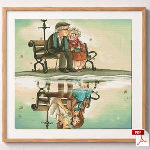 May include: A framed cross-stitch pattern depicting an elderly couple sitting on a park bench, with their reflection in water below showing them as a young couple. The top scene features muted earth tones, while the reflection shows vibrant colors.
