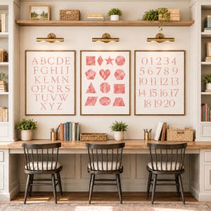 Pode incluir: Três quadros decorativos com gráficos em estilo aguarela rosa. O quadro da esquerda exibe o alfabeto de A a Z, o central mostra várias formas geométricas e o da direita lista os números de 0 a 20 numa fonte clara e legível.