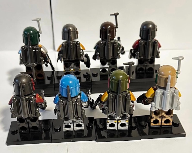 May include: Eight plastic minifigures standing on black rectangular display bases. Each figure wears a helmet and a jetpack, featuring various colour schemes including green, blue, tan, and dark grey, viewed from the back in two rows.