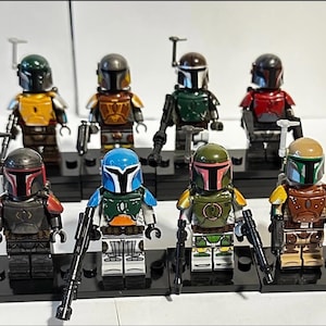 May include: A collection of eight plastic building block minifigures featuring armoured helmets and chest plates in various colours including green, yellow, blue, red, and brown. Each figure stands on a black rectangular base and holds a small black blaster.