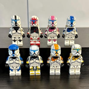 May include: Eight plastic toy soldier minifigures arranged in two rows. Each figure wears a white helmet and armor with distinct color patterns including black, red, pink, blue, yellow, and orange accents, featuring various visor and decal designs.