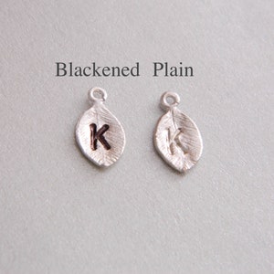 May include: Two silver leaf charms with the letter "K" engraved on them. One charm is plain silver, and the other is blackened.