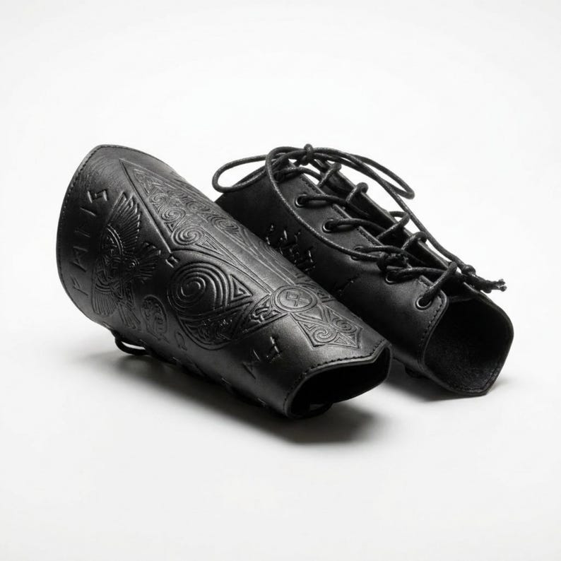 May include: A pair of black leather bracers featuring intricate embossed designs of a bird and geometric patterns, along with runic symbols. The bracers include black cord lacing through metal eyelets for a secure fit around the forearm.