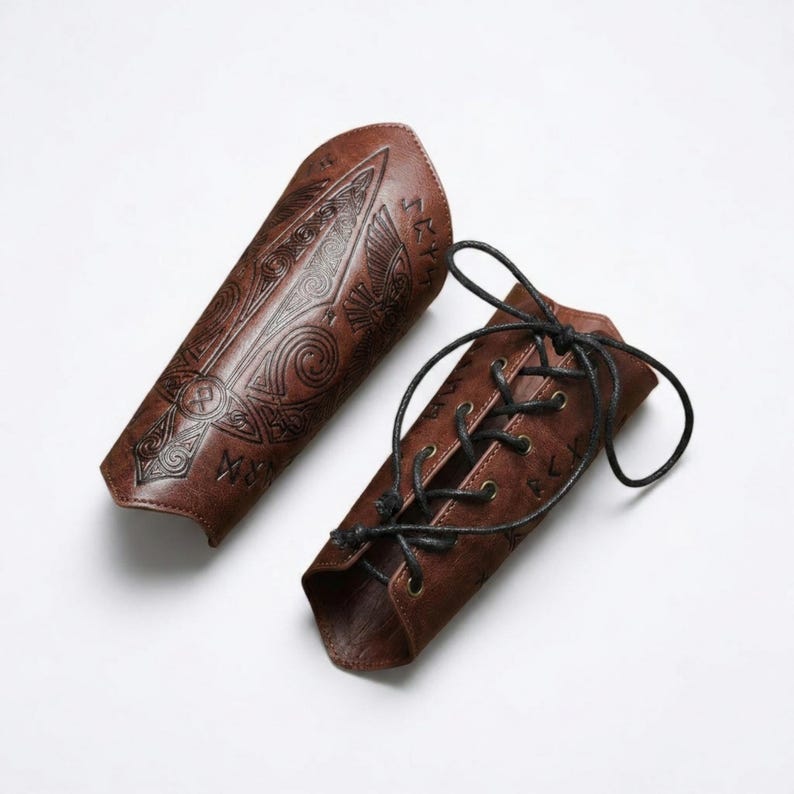 May include: A pair of brown arm bracers featuring embossed intricate patterns, including a central sword motif and runic symbols. One bracer is flat, while the other is curved and secured with black cord lacing through metal eyelets.