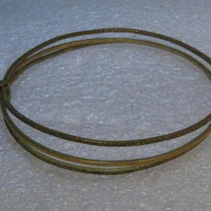 Puede incluir: Un brazalete de doble cadena de color dorado. El brazalete está hecho de metal fino y tiene un diseño simple y elegante.