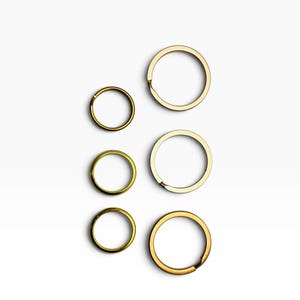 May include: A collection of six circular metal split rings arranged in two vertical columns. The three rings on the left are smaller and have a brass-toned finish, while the three rings on the right are larger and have a polished gold-toned finish.