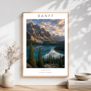 May include: A vertical wall art print featuring a landscape photograph of Banff, Canada. The image displays jagged, snow-capped mountains reflecting in a turquoise lake, framed by evergreen trees under a cloudy sky. Text reads BANFF and CANADA.