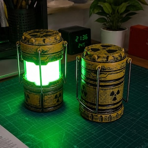 May include: Two cylindrical lanterns with a distressed yellow and black finish, featuring black radiation warning symbols. One lantern emits a bright green light from its center, while the other is unlit. Both have metal handles and textured tops.