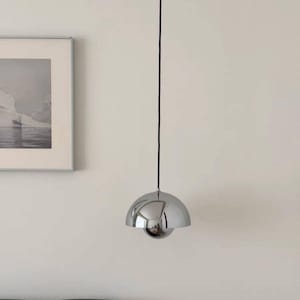 May include: A polished chrome pendant light featuring a spherical design with two nested dome-shaped shades. The fixture is suspended by a thin black cord from the ceiling, reflecting the surrounding environment on its smooth, metallic surface.