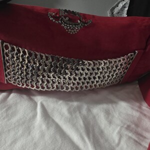 Puede incluir: Un bolso de mano rojo que presenta un panel de malla met&aacute;lica plateada con un patr&oacute;n geom&eacute;trico en la parte frontal. El bolso est&aacute; adornado con un grupo decorativo de cristales transparentes y una piedra roja central sobre la malla met&aacute;lica.