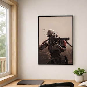 May include: A framed wall art print featuring a soldier in white and red armor aiming a long-barreled rifle with a scope. The figure is positioned in a desolate, rocky landscape under a hazy sky, captured in a realistic, cinematic style.