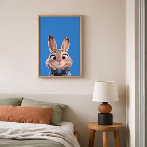 Op de afbeelding: Een ingelijste wandkunstprint met een cartoonkonijn met grote oren, paarse ogen en een lichtbruine en witte vacht, die zijn kin op zijn handen laat rusten tegen een effen blauwe achtergrond, in een lichthouten lijst aan een muur.