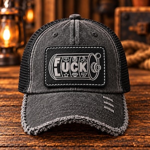 May include: A distressed black trucker hat featuring a rectangular patch on the front. The patch displays a slot machine graphic with the text FUCK and symbols including a clover, skull, cherries, star, diamond, and the number 7.