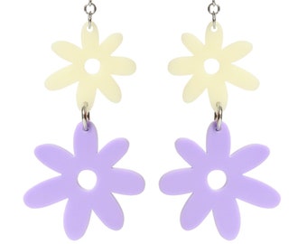 May include: A pair of dangle earrings featuring two layered flower charms. The top flower is a pale yellow and the bottom flower is a light purple.