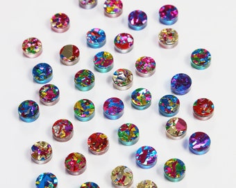 May include: Assortment of colorful round confetti-filled resin cabochons. The cabochons are approximately 1/2 inch in diameter and have a variety of colors, including red, blue, green, gold, and silver.