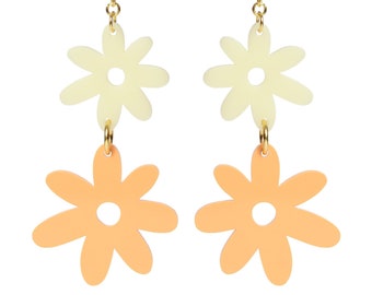 May include: A pair of gold dangle earrings with two layered flower charms. The top flower is white and the bottom flower is peach.
