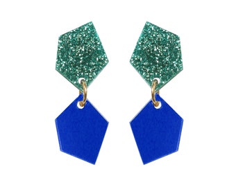May include: A pair of dangle earrings with a blue and green geometric design. The top of each earring is a sparkly green pentagon shape, and the bottom is a solid blue pentagon shape.