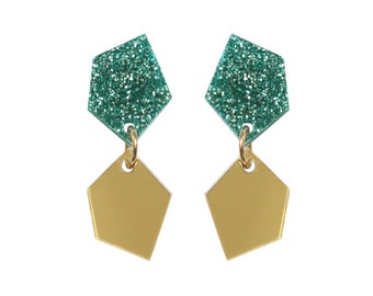 May include: A pair of dangle earrings with a gold and green geometric design. The top of each earring is a green glitter-covered pentagon shape, and the bottom is a gold pentagon shape.