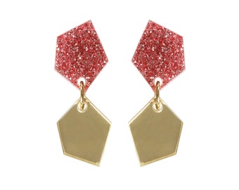 May include: A pair of earrings with a geometric design. The top part of the earrings is a red, glittery pentagon shape. The bottom part of the earrings is a gold, metallic pentagon shape.
