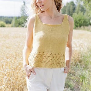 May include: A yellow knitted tank top with a square neckline and a decorative diamond pattern at the hem. The tank top is paired with white pants. The image includes the text "DROPS DESIGN" and the website address.