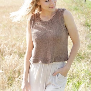 May include: A sleeveless, brown knit top with a rounded neckline and a ruffled hem. The top is paired with light-colored pants. The image includes the text "DROPS DESIGN" and the website address "www.garnstudio.com".