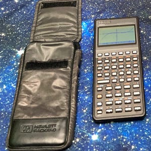 Könnte beinhalten: Ein schwarzer wissenschaftlicher Grafikrechner Hewlett-Packard 48GX mit einem monochromen Flüssigkristall-Display, das eine gezeichnete Kurve zeigt, neben einer passenden schwarzen Stofftasche mit Hewlett-Packard-Logo auf der Vorderseite.