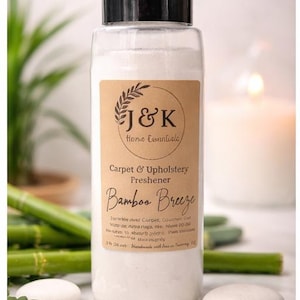 May include: A clear plastic bottle with a black cap containing white powder. The label reads J&K Home Essentials, Carpet & Upholstery Freshener, Bamboo Breeze. It includes instructions and states a net weight of 454 grams. The bottle is cylindrical.