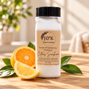 Può includere: Un flacone dosatore in plastica trasparente riempito di polvere bianca, con un'etichetta color cuoio con il testo J&K Home Essentials, Carpet & Upholstery Freshener, Citrus Sunshine e 454 g. Due fette d'arancia e foglie verdi alla base.