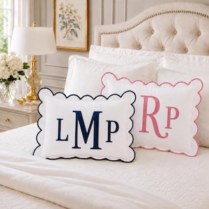 Op de afbeelding: Twee rechthoekige witte sierkussens met geschulpte randen. Eén kussen is voorzien van een donkerblauw geborduurd monogram met de letters LMP, terwijl het andere kussen een roze geborduurd monogram met de letters Rp heeft.