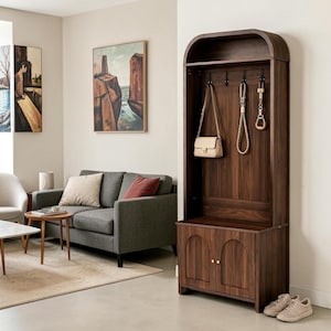 May include: A tall, dark wood hall tree featuring an arched top, an open upper shelf, a back panel with four black metal hooks, and a lower cabinet with two doors. The cabinet doors have vertical wood grain detailing and small gold-toned knobs.
