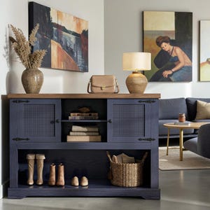 May include: A navy blue wooden console table with a natural wood top, featuring two cabinet doors with mesh panels, an open center shelf with books, and a bottom shelf holding two pairs of boots, a pair of shoes, and a woven basket.