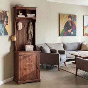 May include: A tall, dark brown wooden hall tree featuring an upper storage shelf, a central panel with three black metal hooks for hanging items, and a lower cabinet with a single door. The cabinet door displays a carved, curved decorative pattern.