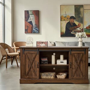 May include: A dark brown wooden media console featuring two sliding barn-style doors with X-shaped accents, black metal hardware, and an open center shelf containing two white cylindrical candles, a small box, and two woven storage baskets.