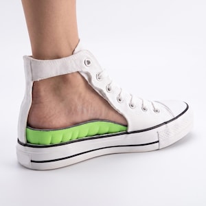 May include: A white high-top canvas sneaker with a cut-out heel design, featuring a bright lime green contoured orthotic insole. The shoe has a white rubber sole with a thin black stripe detail and silver metal eyelets for the white laces.