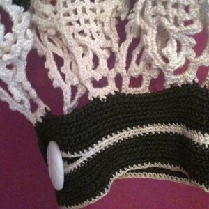 May include: Close-up of a white crocheted fabric with a black and white crocheted trim. A white button is attached to the trim.