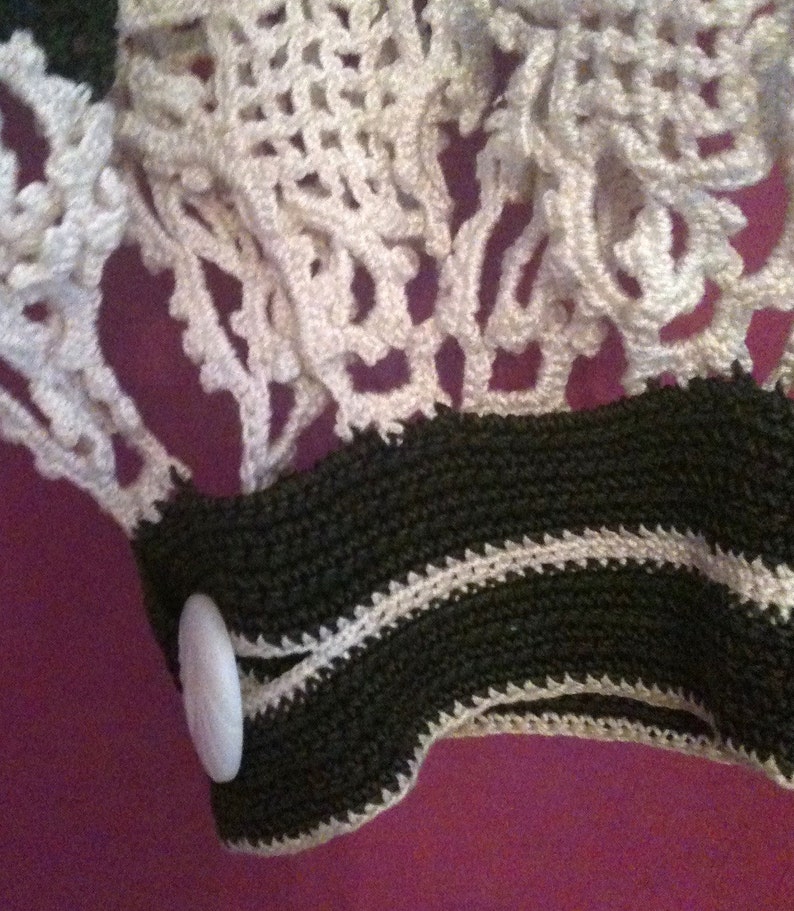 May include: Close-up of a white crocheted fabric with a black and white crocheted trim. A white button is attached to the trim.