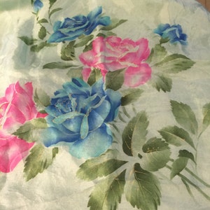 May include: A light green fabric with a floral pattern featuring pink and blue roses with gold accents. The roses are painted on a light green background.