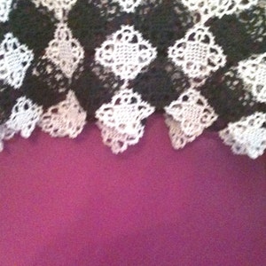 May include: Black and white crocheted lace fabric with a checkered pattern. The fabric has a scalloped edge.