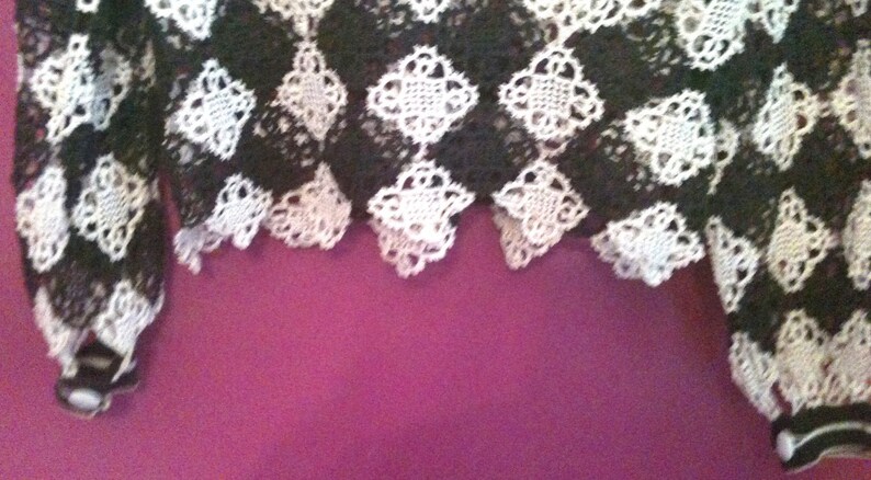 May include: Black and white crocheted lace fabric with a checkered pattern. The fabric has a scalloped edge.